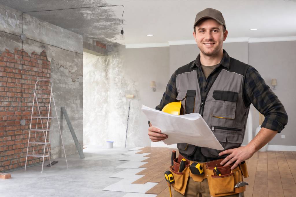 Artisan de l’entreprise Art Bat tenant des plans dans une maison en cours de rénovation, avec travaux de maçonnerie et pose de parquet.